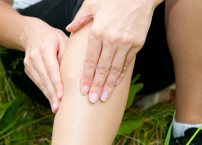 A person with their hands on the front of one leg, holding their shin.